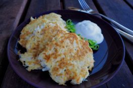 Potato pancakes on a dark plate with green onion and sour cream
