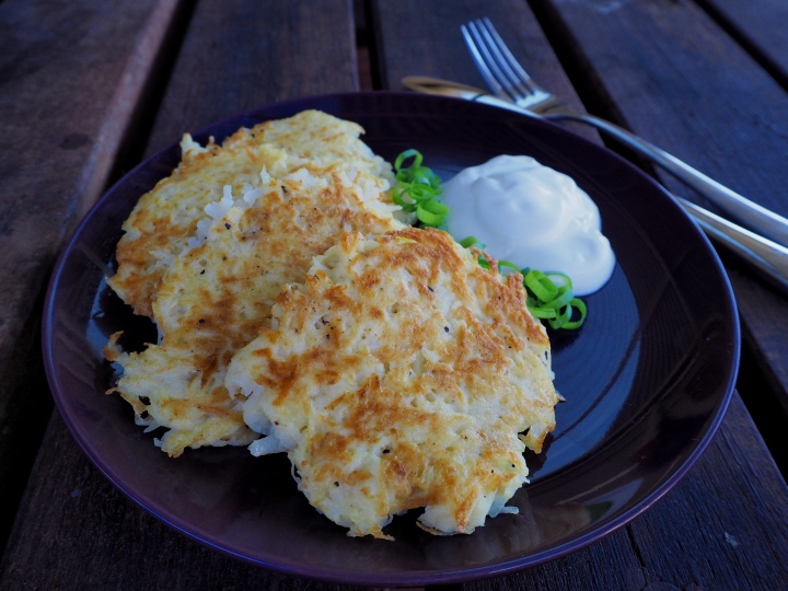 Potato pancakes on a dark plate with green onion and sour cream