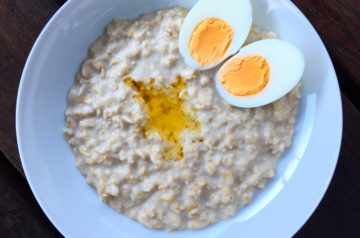 Oatmeal porridge on a white plate with butter and hard boiled eggs