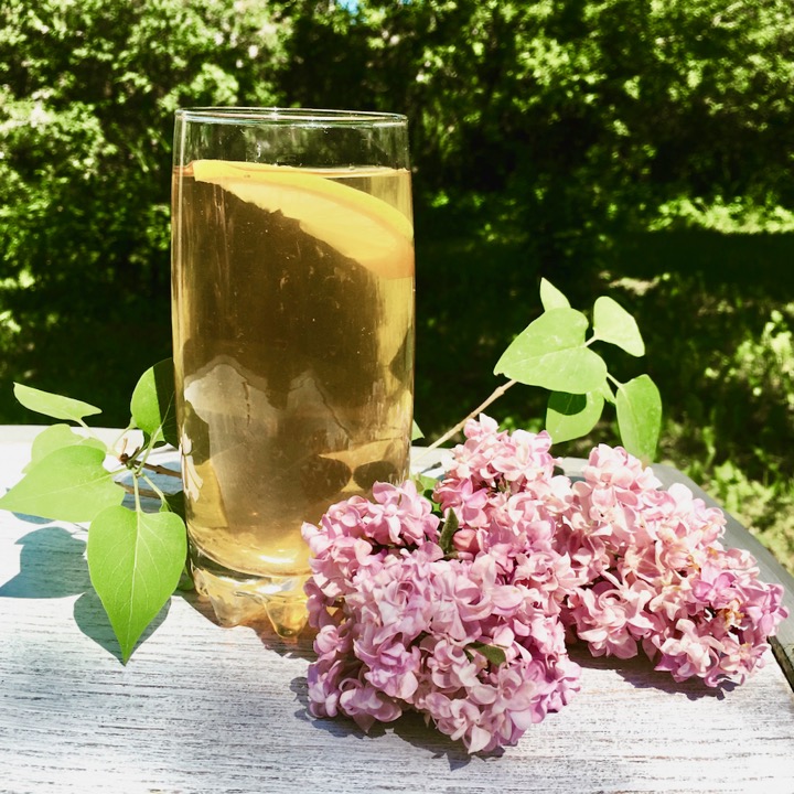 glass of ice tea on white chair with purple lilacs