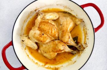 Roast chicken in red cast iron pan on white background