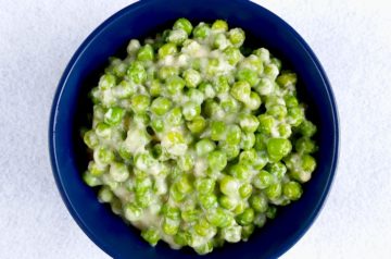 Sauteed green peas in white sauce in a blue bowl on white background
