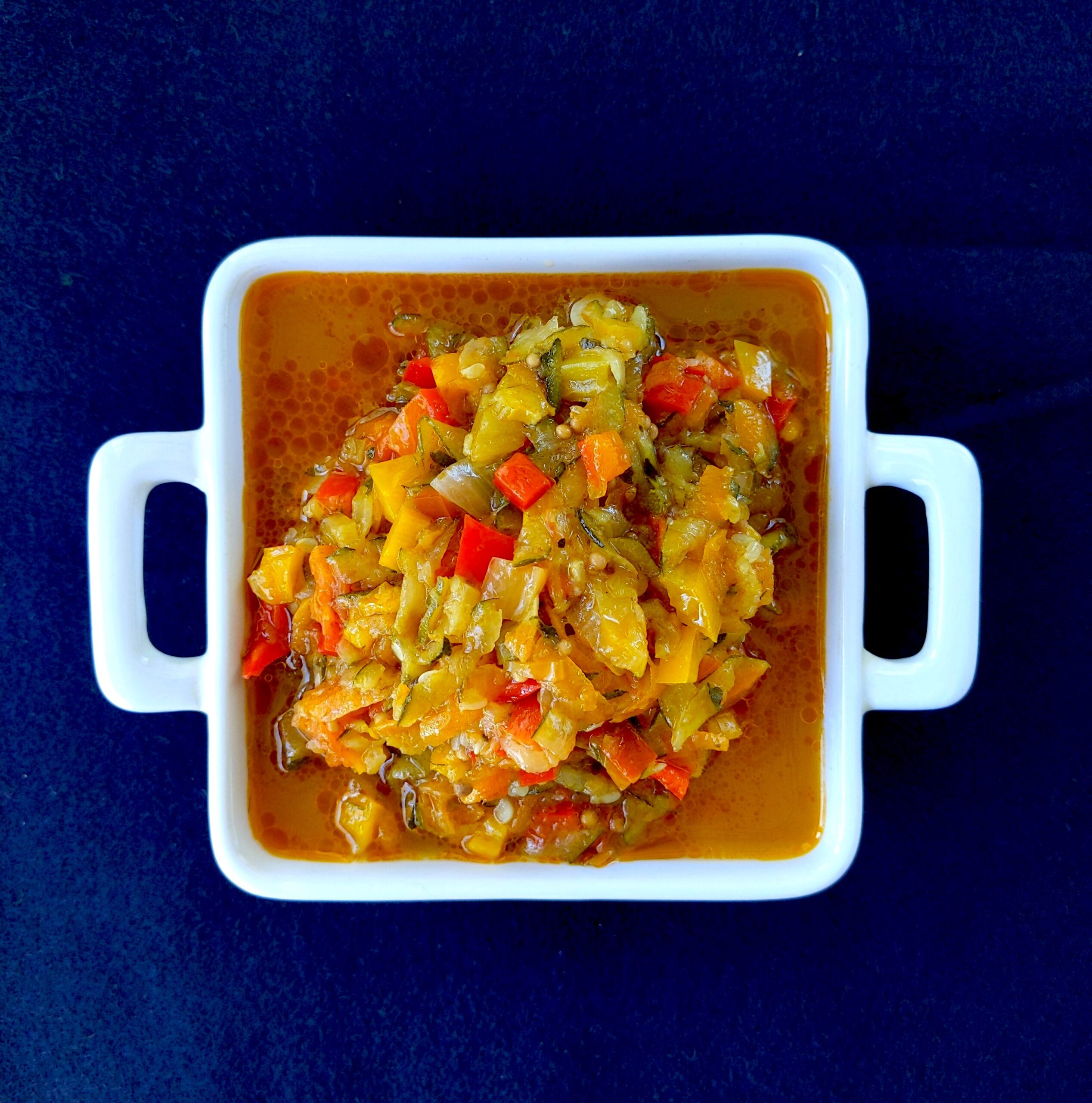 Zucchini relish in a white square dish on a maroown background