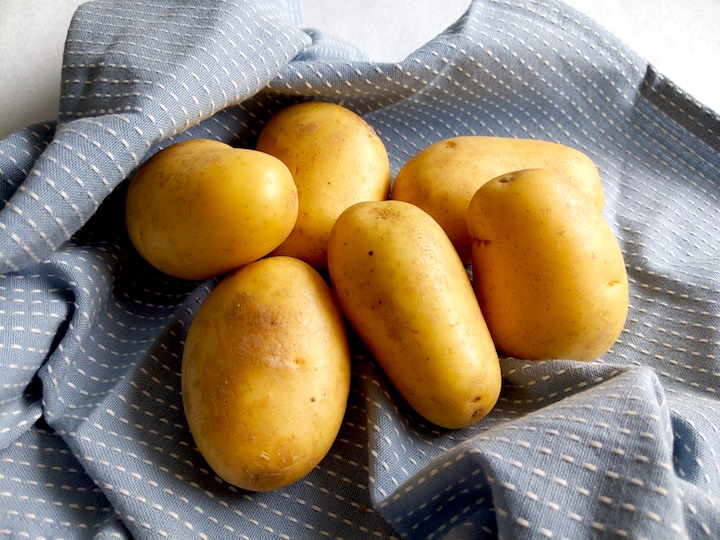 Yellow raw potatoes on a blue tea towel
