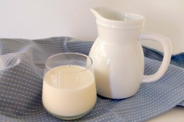 Glass of milk and a white jug on a blue tea towel on white background