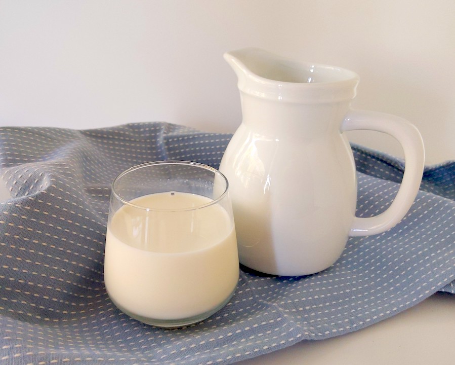 Glass of milk and a white jug on a blue tea towel on white background