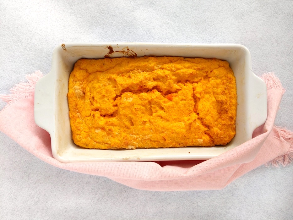 Carrot pudding in a white baking dish on a pink and white background